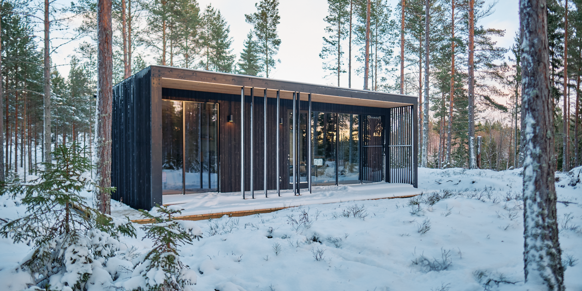 Swedish forest cabin with black charred timber exterior and floor-to-ceiling windows surrounded by snow-covered pine trees